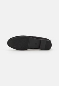 Black suede shoe sole features a textured rubber bottom with geometric patterns for grip and durability. Rounded toe with slight heel.