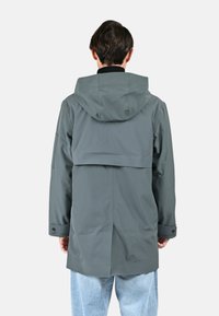 Veste imperméable grise avec capuche, offrant un design à dos évasé et des poignets réglables, fabriquée en matériau synthétique lisse.