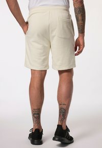 Shorts beige clair en tissu doux, dotés d'une poche arrière et d'une coupe décontractée, vus de l'arrière avec des chaussures de sport noires.