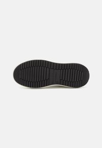 Semelle de chaussure en caoutchouc noir avec des rainures horizontales profondes et le nom de la marque "Marc O'Polo" embossé au centre sur fond blanc.