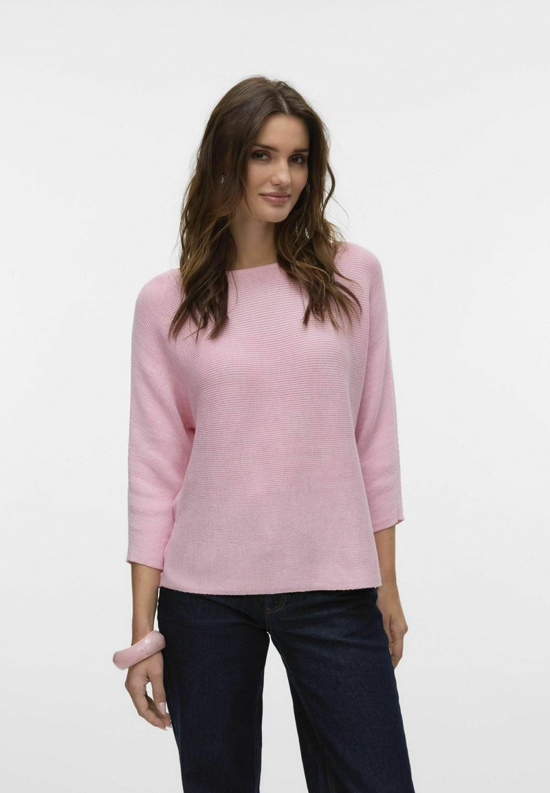Maglione a coste rosa chiaro con maniche a tre quarti, scollatura ampia e orlo dritto. Abbinato a jeans blu scuro e un semplice bracciale.