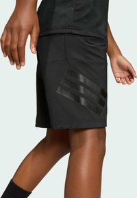 Crne atletske kratke hlače s glatkom teksturom, koje imaju tri sjajne horizontalne pruge na lijevoj nozi i prilagođeni kroj.