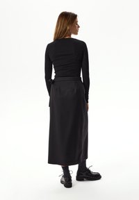 Czarna dopasowana bluzka z długim rękawem i okrągłym dekoltem, zestawiona z długą czarną spódnicą z wiązaniem w talii oraz błyszczącymi czarnymi butami na sznurowadła.