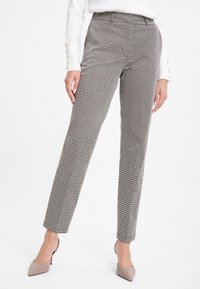 Pantalons à motif gris avec une coupe droite. Présente un tissu texturé et une taille plate, portés avec des chaussures à talons beiges.