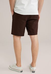 Pantalones cortos marrones de corte recto y con dobladillos, combinados con zapatillas de lona de color claro, vistos desde atrás.