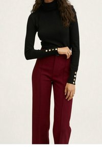 Pull à col roulé noir avec des boutons dorés sur les manches, associé à un pantalon bordeaux taille haute avec une coupe ajustée et un tissu lisse.
