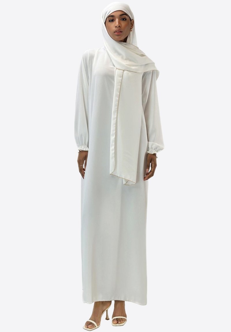 Longue robe blanche à silhouette fluide, manches bouffantes et foulard assorti. Tissu lisse avec un léger éclat. Design simple.