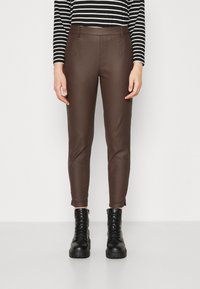 Pantalon en simili cuir marron à coupe ajustée, avec des poches avant et une texture lisse, associé à des bottines noires à lacets.