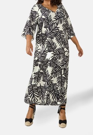 Femme portant une longue robe à motifs de feuilles noires et blanches avec des manches trois-quarts et des espadrilles compensées noires à lacets à la cheville.