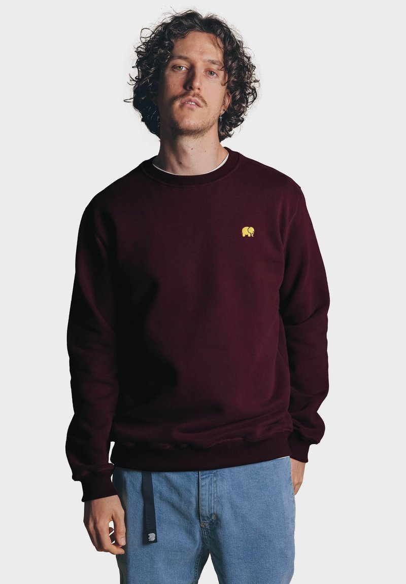 Vínový svetr vyrobený z měkkého materiálu, s malým žlutým logem slona na levé hrudi, s žebrovanými manžetami a spodním lemem.