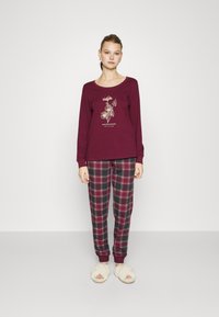 Bordeaux lange mouwen top met bloemenafbeelding en tekst, gecombineerd met geruite broeken in bordeaux, groen en wit, met een omgeslagen zoom. Witte donzige slippers.