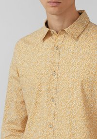 Geel overhemdd met knopen, voorzien van een bloemenpatroon, standaardkraag en beige knopen, gemaakt van een lichte stof met een licht gestructureerde afwerking.