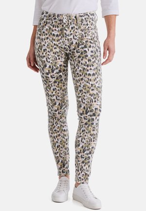 Schmal geschnittene Hosen in Grün, Schwarz und beigem Leopardenmuster, kombiniert mit weißen Sneakern und einem weißen Oberteil.