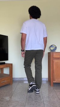 Calças verdes-oliva com corte slim, combinadas com uma t-shirt branca. Ténis Nike em preto e branco. Mobiliário de madeira ao fundo.