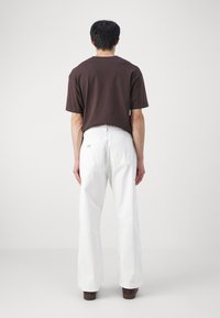 Bruine T-shirt met korte mouwen en een relaxte pasvorm, gecombineerd met witte wijde broek. Opvallende details van achterzakken en eenvoudige stiksels.
