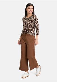 Top con stampa animale in beige e nero, abbinato a pantaloni larghi marroni e sneakers bianche. Presenta maniche 3/4 e scollatura rotonda.
