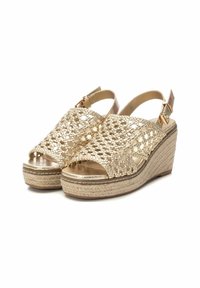 Sandalias de cuña doradas con parte superior trenzada, punta abierta y tira de tobillo. Plataforma envuelta en yute para textura y altura. Plantilla metálica suave.