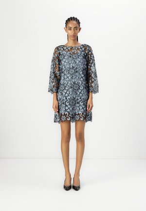 Blonde blonde blonder knipling dress med blå blomsterdesign, trekvart ermer, scalloped hem, kombinert med svarte høyhælte sko, modell står mot hvit bakgrunn.