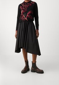 Black sweater with red floral embroidery, paired with a black pleated skirt, and brown Chelsea boots with a chunky sole and black elastic sides.