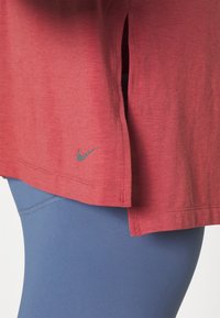 Camisa roja de manga corta con aberturas laterales y un logo gris de Nike, combinada con leggings azules que presentan una textura suave y un diseño ajustado.