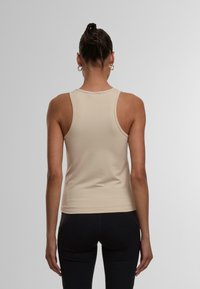 Beige enganierter Tanktop mit einem runden Ausschnitt und breiten Trägern, aus einem weichen, dehnbaren Stoff gefertigt. Keine sichtbaren Muster.