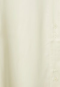 Camicia gialla chiaro con bottoni, realizzata in tessuto liscio, caratterizzata da bottoni distribuiti in modo uniforme e un design semplice con una leggera lucentezza.