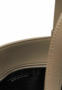 Primo piano dell'interno di una borsa in pelle beige con una cerniera visibile e un'etichetta in tessuto nera che recita "A|X Armani Exchange."