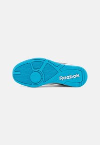 Reebok-sneaker sula i blå gummi med texturerat mönster. Har varumärkets logotyp i vitt och cirkulärt greppdetalj.