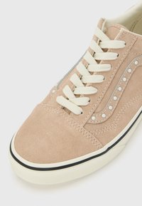 Baskets en daim marron clair avec lacets blancs, semelle en caoutchouc blanche, et coutures décoratives ainsi que rivets sur le panneau latéral.