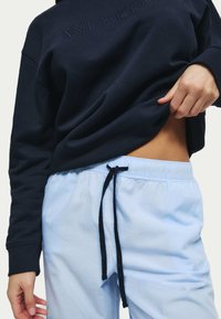 Marinblå sweatshirt med embossat "WEEKEND", tillsammans med ljusblå dragkedjegylfbyxor. Sweatshirten har ribbad mudd; byxorna har en avslappnad passform.