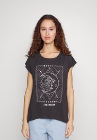 Mørk grå t-skjorte med løs passform, med et hvitt grafisk design av en måne og ansikt, omkranset av geometriske mønstre og teksten "THE MOON."
