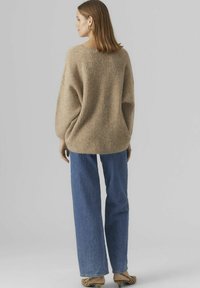 Beige stickad tröja med avslappnad passform och vida ärmar, kombinerad med ljusblå högmidjade jeans och klackar med djurmönster.