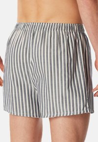 Boxers rayés en bleu, blanc et gris. Ceinture élastique, coupe ample, longueur mi-cuisse. Tissu doux avec un motif à rayures verticales.