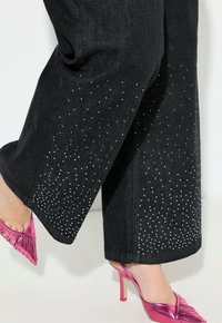Pantaloni in denim neri a gamba larga con una gradazione di borchie argentate ai orli. Abbinati a scarpe con tacco alto rosa lucido con dettagli plissettati.