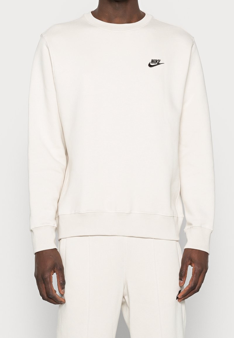 Sudadera de un beige claro hecha de una tela suave, con cuello redondeado y puños acanalados. Logo negro de Nike bordado en el pecho.
