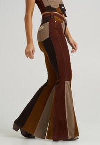 Flared corduroy pants featuring a patchwork design in brown, rust, beige, and olive colors, with prominent side seams and back pockets.