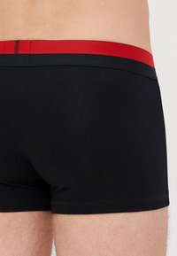 Schwarze Boxershorts mit einem roten elastischen Bund, aus einem glatten, dehnbaren Stoff mit enger Passform. Keine zusätzlichen Muster oder Akzente.