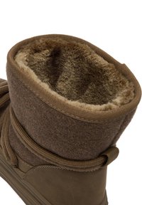 Brązowy zimowy but z miękkim, puszystym futrem wewnątrz, fabrycznym mankietem i widocznymi detalami szwów podeszwy, uchwycony z bliska pod kątem.