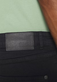 Mustad musta denimi püksid tekstureeritud musta nahast plaadiga, millel on kiri "DENIM JOURNEY." Omavad peent tikandit ja klassikalist viit taskut.
