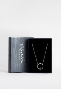 Collana in argento con un pendente circolare e un piccolo dettaglio di design, presentata in una scatola per gioielli di colore blu scuro e texture.