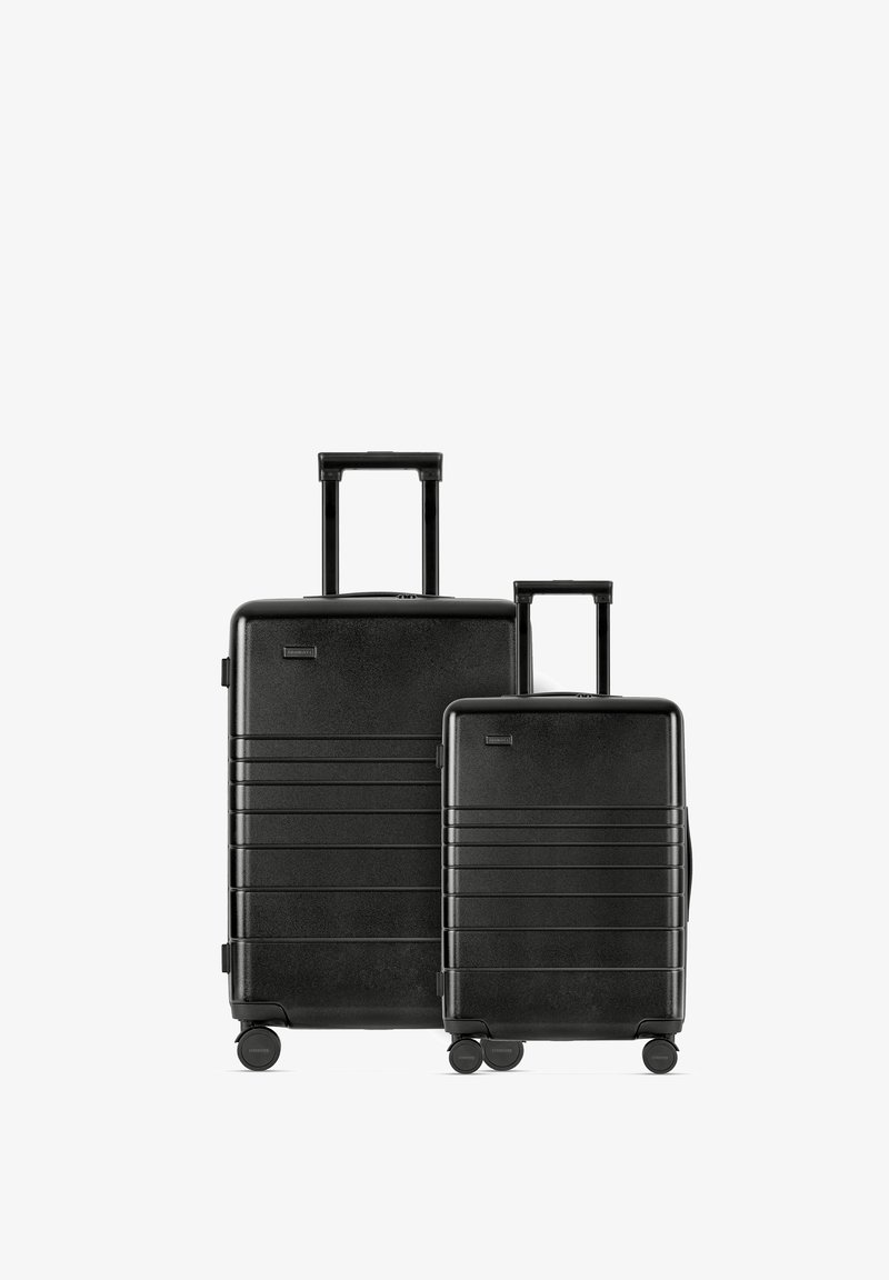 Twee zwarte harde koffer van verschillende maten, met horizontale lijnen, uitschuifbare handvatten en elk vier wielen voor eenvoudige mobiliteit.