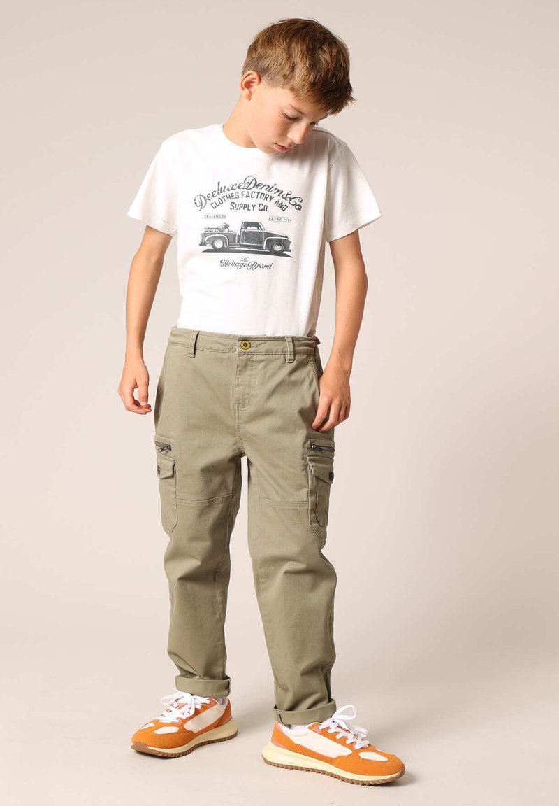 Witte T-shirt met grafische print; olijfgroene cargo broek met zijzakken; oranje en witte sport sneakers met een gestructureerde zool.