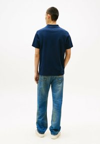 Polo de color azul marino con mangas cortas, hecho de una tela suave. Combinado con unos jeans de color azul claro con un ligero desgaste y bolsillos traseros.