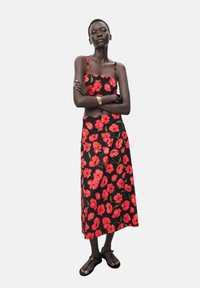 Black floral dress featuring red hibiscus patterns, spaghetti straps, and a maxi length. Worn with flat black sandals and basic jewelry accents.