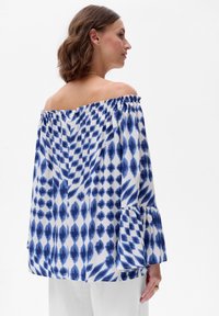 Bluzka na jedno ramię w niebiesko-białym kolorze, z wzorzystym deseniem, puffowanymi rękawami i zebranym dekoltem, wykonana z lekkiego materiału.