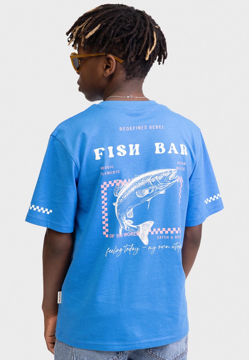 Camiseta de algodón azul con un estampado gráfico de un pez, detalles de cuadros y texto en la parte posterior. Mangas cortas y un diseño de ajuste relajado.