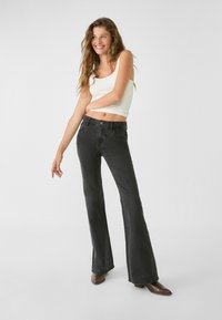 Jeans neri svasati con vita media, dotati di cinque tasche, cuciture tono su tono e una leggera texture di lavaggio, abbinati a un top leggero senza maniche.