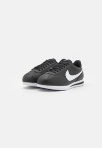 Tenisi negri din piele cu vârf rotund, cu logo-ul alb Nike Swoosh, șireturi negre și talpă din cauciuc albă, având o suprafață texturată și un design sportiv.