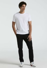 Witte katoenen t-shirt met het logo van "Original Penguin" in lichte borduursel, gecombineerd met zwarte jeans en witte sneakers.