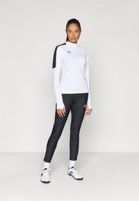 Long-sleeve white athletic top with black and neon green accents, paired with slim-fit black pants and white athletic shoes.